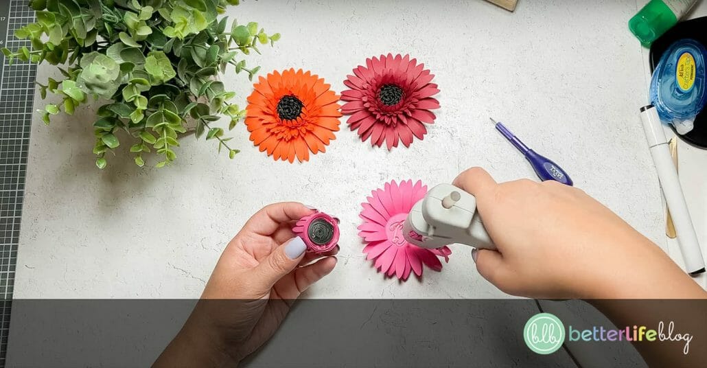 Adding hot glue to the center of a piece of pink cardstock in the shape of a gerbera daisy