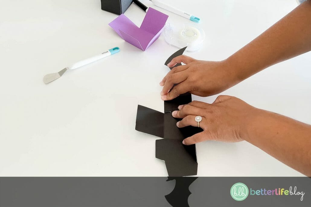 Folding black cardstock cut out into a shape of a bat treat box by a Cricut machine