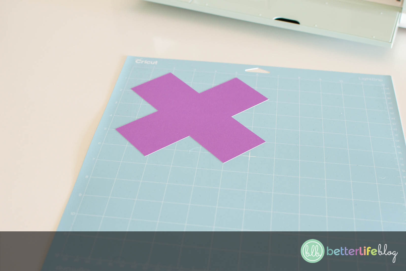 A piece purple cardstock in the shape of an "x" on a light grip mat