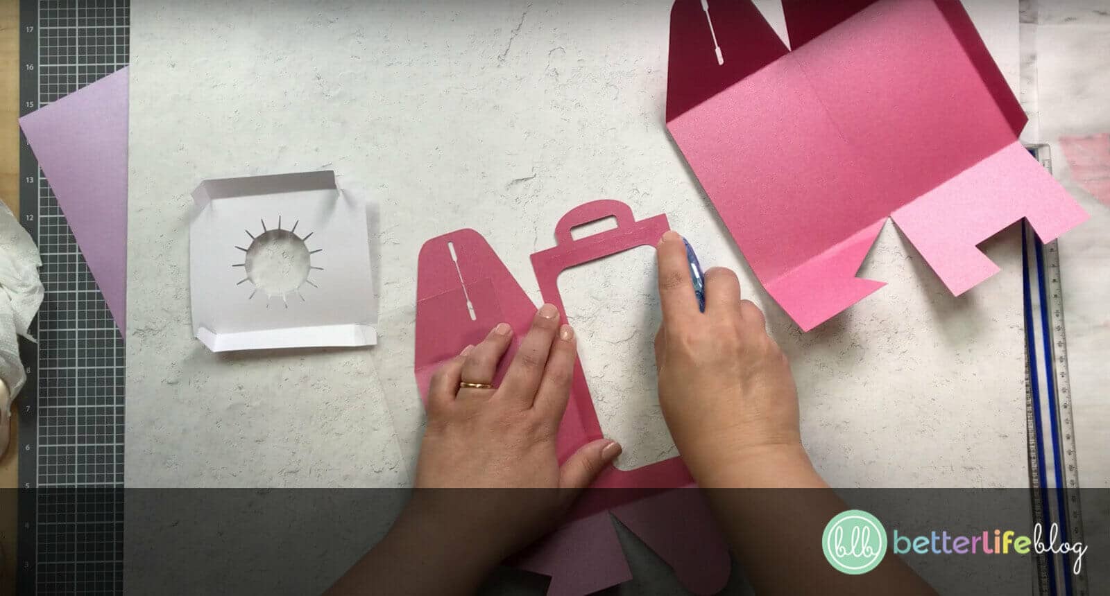 Adding crafter’s tape to the edge of a pink piece of cardstock cut out by a Cricut