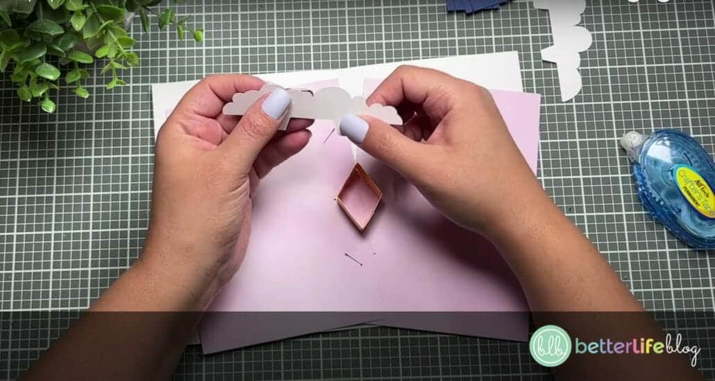 Folding a piece of white cardstock that’s in the shape of a cloud