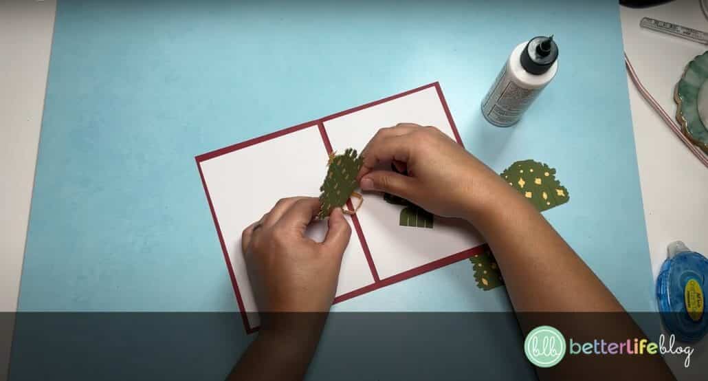 Assembling pieces of green and yellow cardstock, shaped as trees, to make a Cricut Christmas Pop-Up Card
