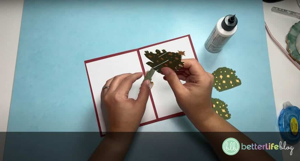 Assembling pieces of green and yellow cardstock, shaped as trees, to make a Cricut Christmas Pop-Up Card