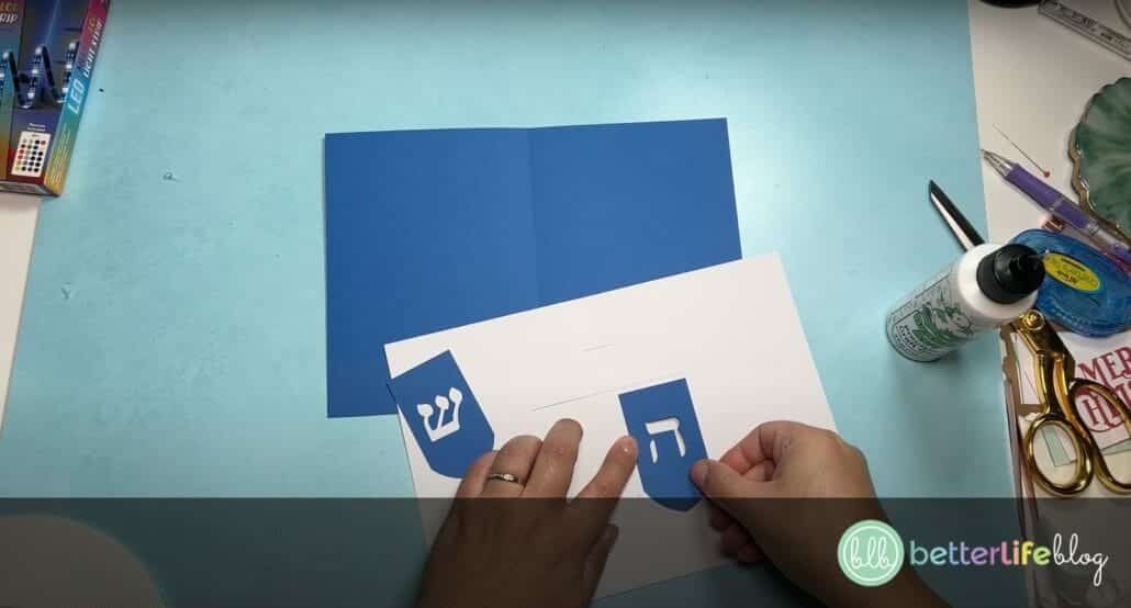 Adding a piece of blue cardstock onto a white piece of cardstock to make a Hanukkah-themed greeting card