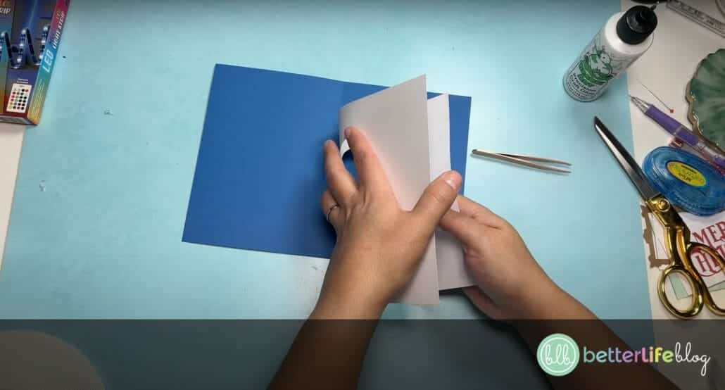 Folding white cardstock with a large piece of blue cardstock lies in the background